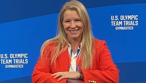 Dr. Lancaster sitting in front of blue Olympics banner.